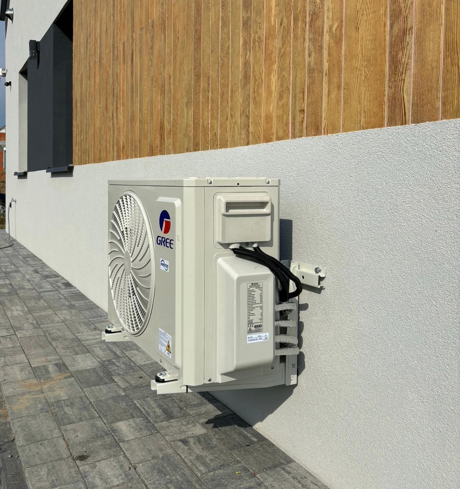 Outdoor Gree air conditioning unit mounted on a white and wood-paneled building wall above gray concrete pavement.